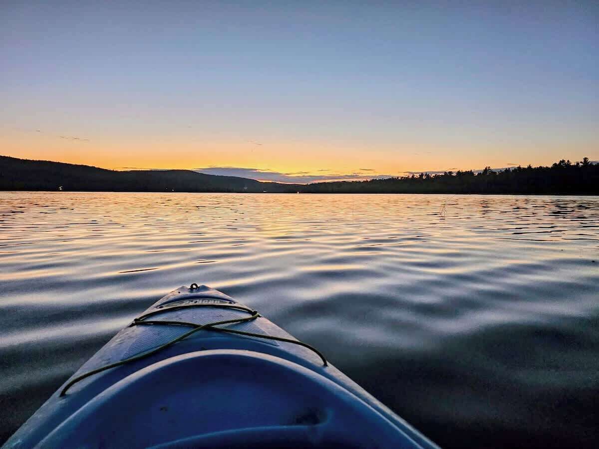 Een kajak op kalm water, met een zonsondergang op de achtergrond.