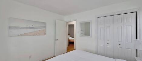 A bedroom with a bed, a door, a mirror, and a painting on the wall.