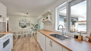 Et moderne køkken med hvide skabe, en træbordplade, en vask og et spiseområde med et hvidt bord og stole.