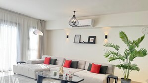 Una sala de estar moderna con un sofá seccional, una mesa de centro, una planta en maceta y un aire acondicionado instalado en la pared.