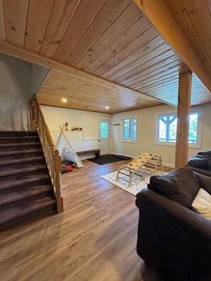 A spacious loft with a wooden staircase, a black leather sofa, a wooden ceiling, and a view of the outdoors.