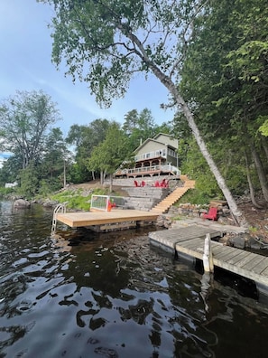 A house on stilts over water with a dock, surrounded by trees.