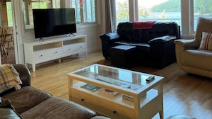 Een woonkamer met een televisie, leren banken, een salontafel en grote ramen met uitzicht.