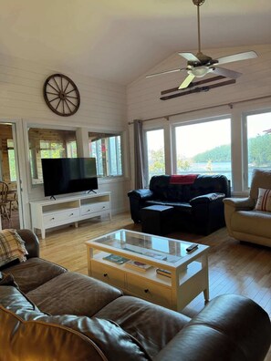 A living room with a TV, leather sofas, a coffee table, and large windows with a view.
