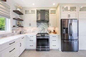 Une cuisine moderne avec des armoires blanches, un réfrigérateur en acier inoxydable, une cuisinière à gaz et un four à micro-ondes.
