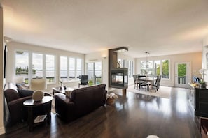 A spacious living area with a fireplace, large windows, and a dining area.