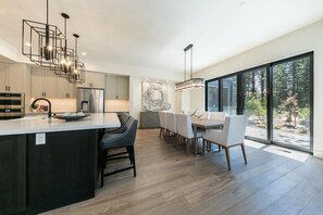 A modern kitchen with a central island, dining area with chairs, and large windows. - 10248 Modane Place-Golf Access & Club Amenities! (Truckee)