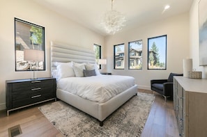 A modern bedroom with a large bed, bedside tables, a desk, and a chair. - 10248 Modane Place-Golf Access & Club Amenities! (Truckee)