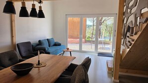 Un espai de vida modern amb zona de menjador, un sofà blau i vistes a una terrassa exterior a través de grans portes de vidre.