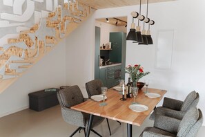 Un espace repas comprenant une table en bois, des chaises à revêtement gris et un escalier avec une rampe en bois.