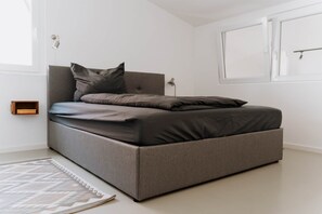 Une chambre moderne avec un canapé-lit gris, un tapis à motifs et une lampe de chevet.