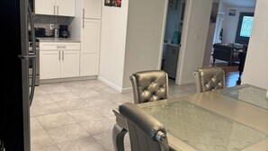 Una cocina moderna con armarios blancos, un refrigerador de acero inoxidable y un comedor con una mesa de vidrio y sillas de cuero.