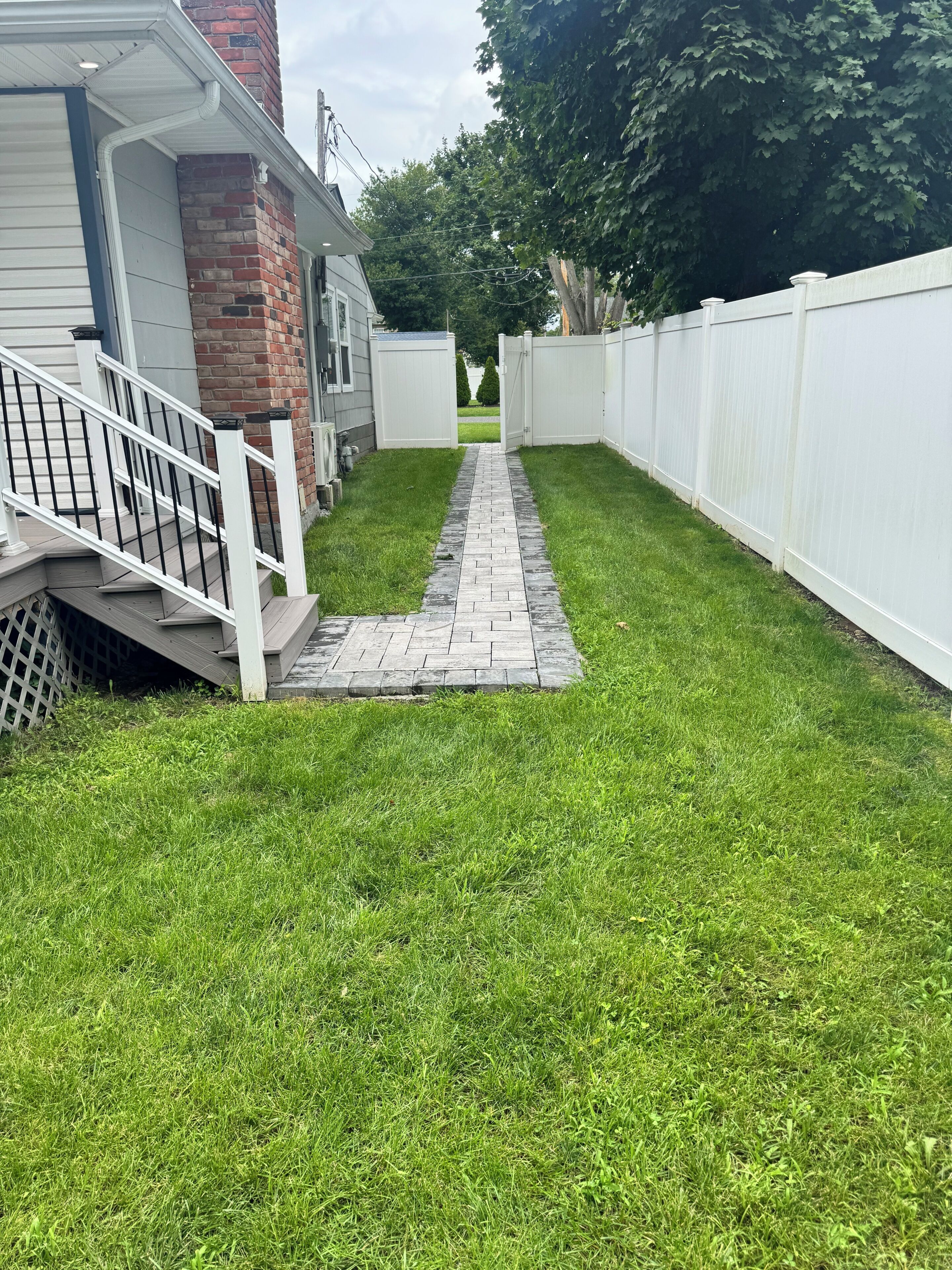 A pathway leading to a gated area with a brick house and a white fence.
