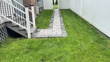 A pathway leading to a gated area with a brick house and a white fence.