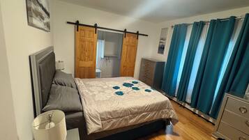 A bedroom with a bed, a dresser, a nightstand, a lamp, a wardrobe, and a ceiling light.