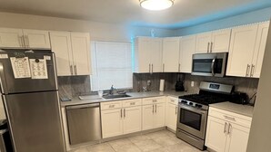 Una cocina moderna con armarios blancos, electrodomésticos de acero inoxidable y piso de baldosas.