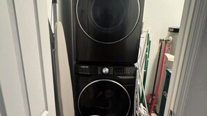 Un cuarto de lavandería con lavadoras y secadoras apiladas, una cesta de ropa y productos de limpieza.