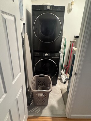 A laundry room with stacked washers and dryers, a laundry basket, and cleaning supplies.