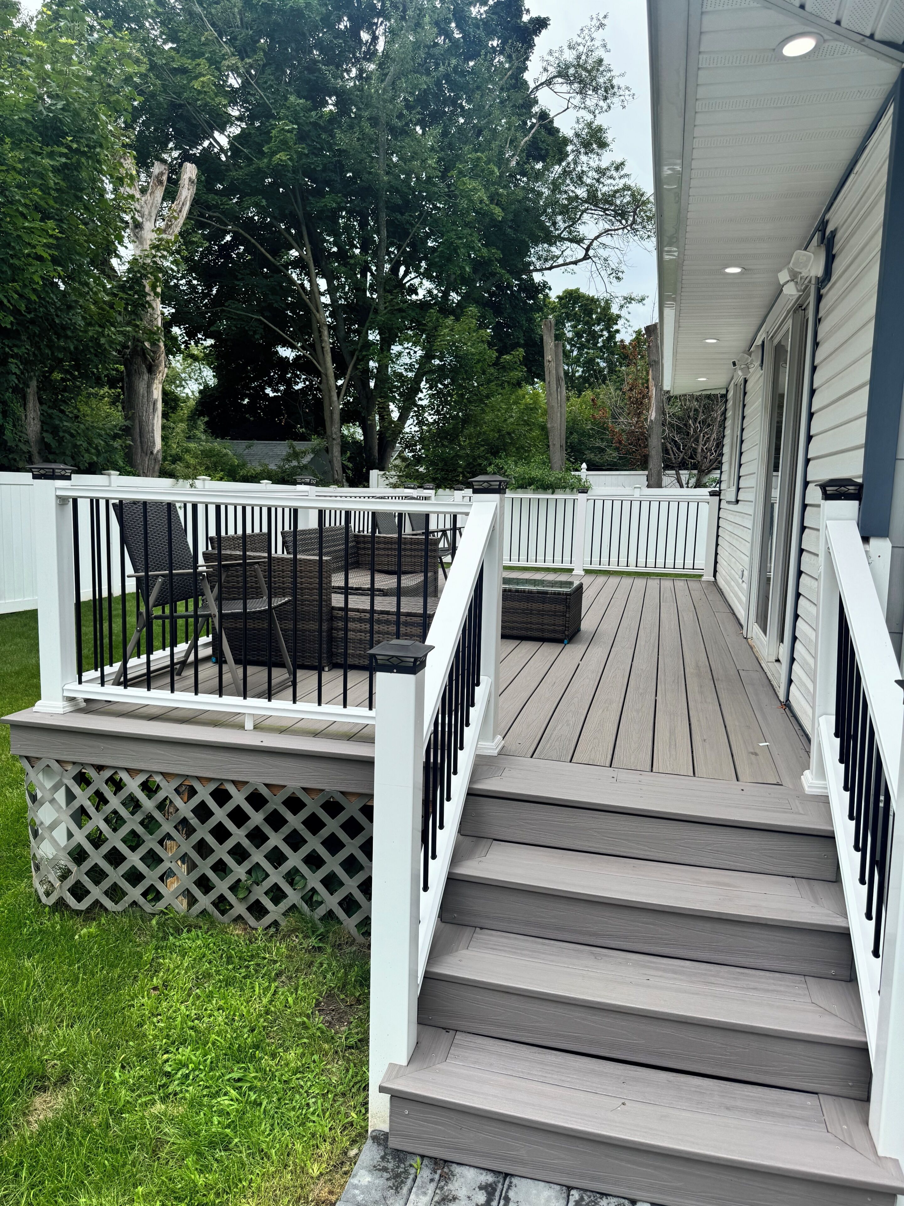 A wooden deck with a white railing, a set of stairs, and outdoor furniture.