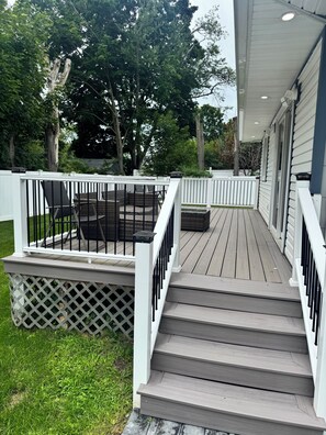 Een houten terras met een witte balustrade, een trap en tuinmeubilair.