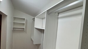 Un pasillo estrecho con piso de madera, paredes blancas y un armario empotrado con estantes y espacio para colgar.