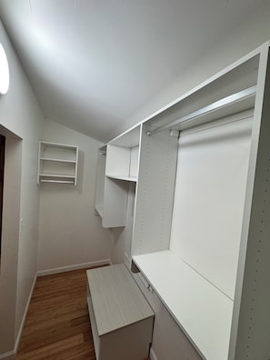 A narrow hallway with a wooden floor, white walls, and a built-in closet with shelves and hanging space.