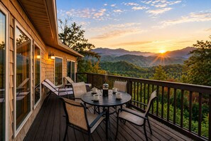 Eine Terrasse mit Tisch und Stühlen, die auf eine gebirgige Landschaft bei Sonnenuntergang blickt.