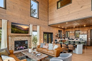 Amplia sala de estar con chimenea de piedra, sofá de cuero y zona de comedor con cocina al fondo.