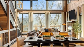 Un intérieur moderne comprenant un coin repas, un ensemble de canapés et de grandes fenêtres donnant sur la verdure.