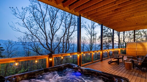 Un bain à remous sur une terrasse en bois, agrémentée de guirlandes lumineuses, avec vue sur une zone boisée.