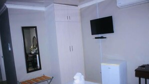 A hotel room with a bed, a television mounted on the wall, a wardrobe, and a small desk with a chair. - The Empire Inn (Serowe)