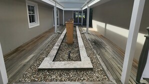 A narrow courtyard with a central planter, wooden deck, and a covered area with a sloped roof.