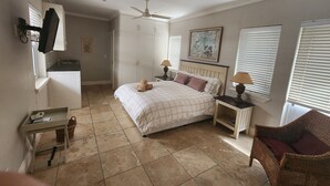 A bedroom with a bed, two bedside tables, a ceiling fan, a window with blinds, and a wall-mounted TV.