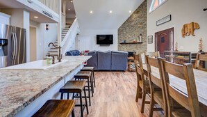 A modern kitchen with a marble countertop, wooden stools, a gray sofa, and a stone wall. - Cranmore Heights | Luxe, Hot Tub, Walk Downtown (North Conway)