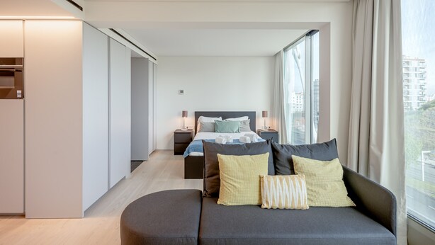 A modern hotel room with a bed, a sofa, and a large window with a city view. - Areeiro Vision Studio by Homing (Lisbon)