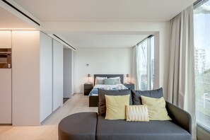 Ett modernt hotellrum med en säng, en soffa och ett stort fönster med utsikt över staden.