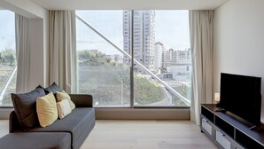 A modern living room with a sofa, a TV, and a large window with a view of buildings and a bridge. - Areeiro Vision Studio by Homing (Lisbon)