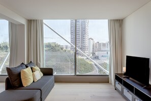 A modern living room with a sofa, a TV, and a large window with a view of buildings and a bridge. - Areeiro Vision Studio by Homing (Lisbon)