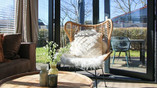 A modern interior with a wicker chair, a cushioned sofa, and a wooden table with a vase and candle. - The Kingfisher is a comfortable ground-floor bungalow with fenced garden, wood stove and fully equipped kitchen. Near the beach, dunes and forest of Schoorl, Petten and Bergen. Perfect for families and dog lovers. (Dirkshorn)