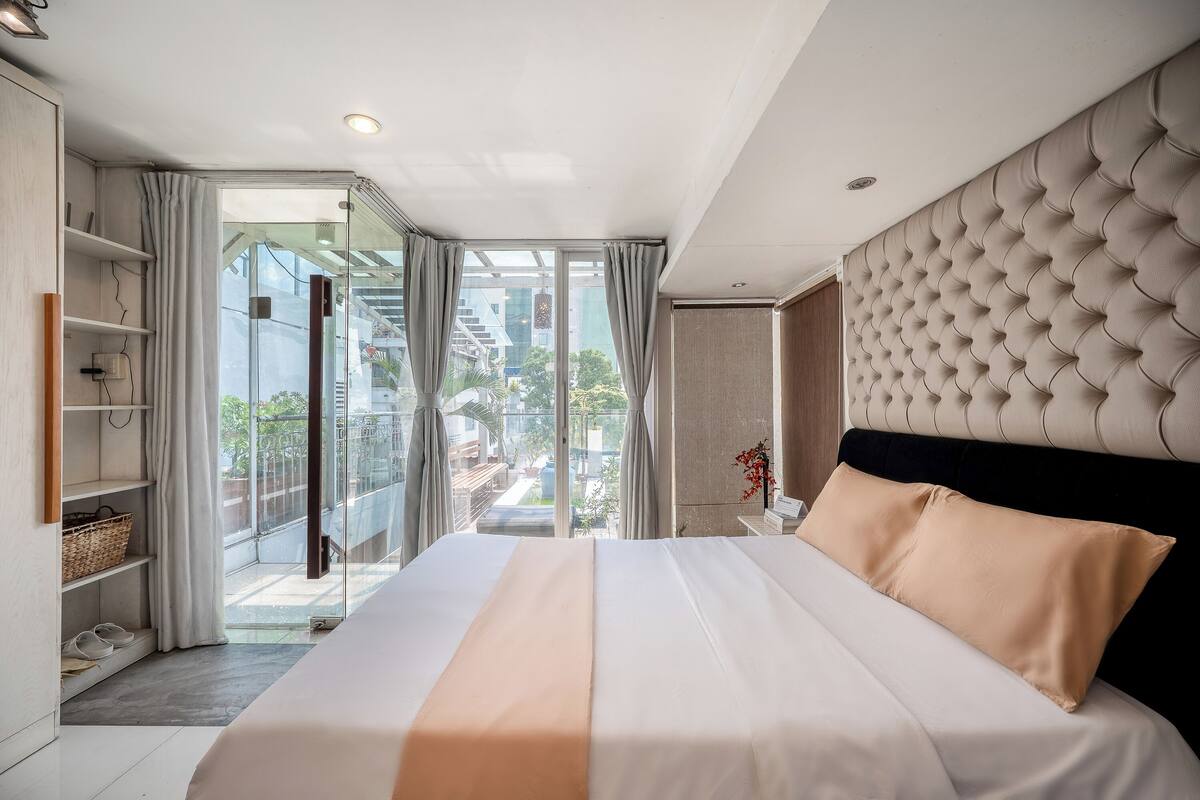 A hotel room with a large bed, a glass door leading to a balcony, and a view of the outside.