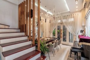 Un intérieur moderne avec un escalier, un coin repas et de grandes fenêtres.