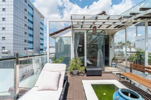 Une terrasse sur le toit, dotée d’une structure vitrée, avec une piscine, des chaises longues et des plantes en pot.