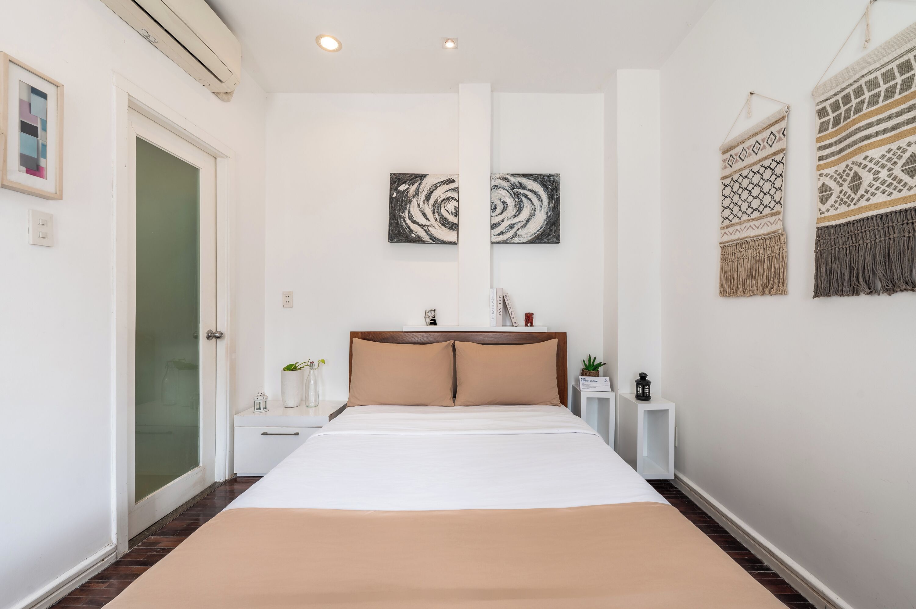 Un dormitorio con cama, una mesita de noche, aire acondicionado de pared y dos cuadros.