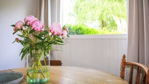 Una mesa de madera con un jarrón de flores, un cuenco y una ventana que da a vistas de vegetación.