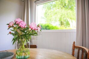 Ein Holztisch mit einem Blumenstrauß, einer Schale und einem Fenster mit Blick auf Grünfläche.