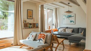 Una sala de estar con un sofá, una silla, una estantería y un ventanal con cortinas.