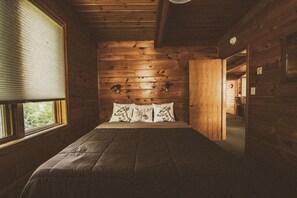 A wooden cabin bedroom with a bed, pillows, and a window.