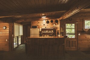 Een rustiek houten interieur van een blokhut, met een keukenhoek voorzien van een koelkast, fornuis en hangende pannen.