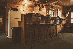 A rustic kitchen with wooden walls, a refrigerator, and bar stools.