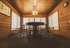 Un intérieur en bois avec une table ronde, des chaises, un luminaire suspendu et une horloge au mur.